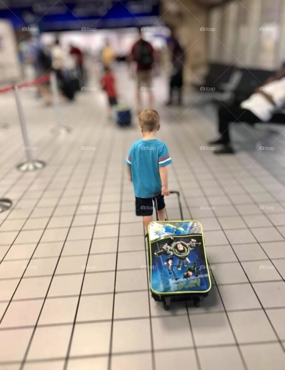 A young boy pulls his Buzz Lightyear, Toy Story, suitcase walking through a busy airport. 