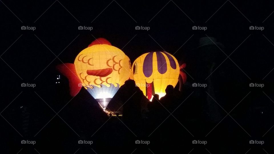 Two fish themed hot air balloons "kiss" while lit up at night