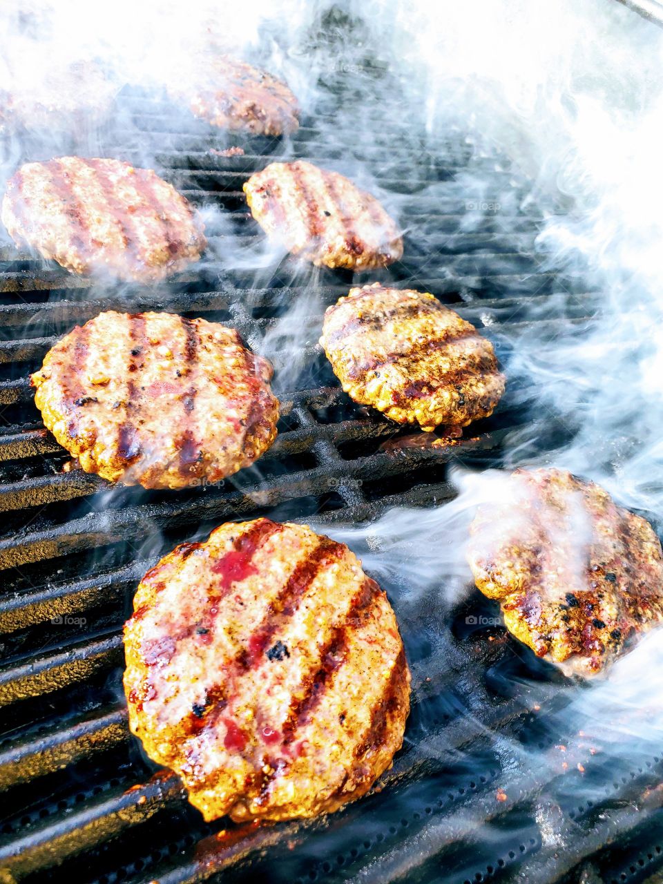 Delicious hamburgers steam on the barbecue grill during a summer cookout
