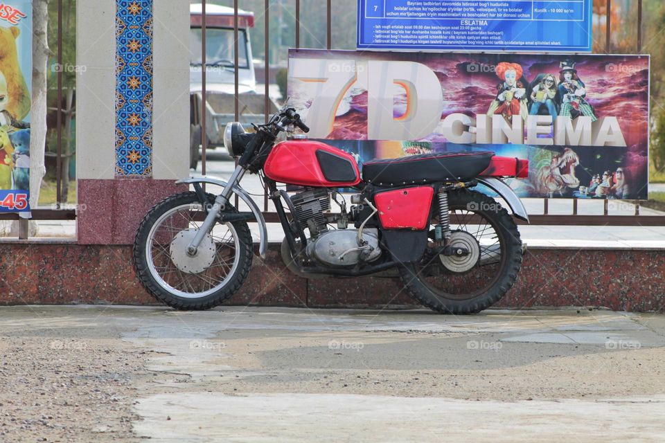 an ordinary old motorcycle stands by the fence