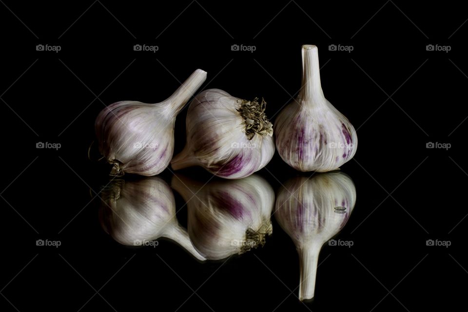 Three heads of garlic on a black background with reflection