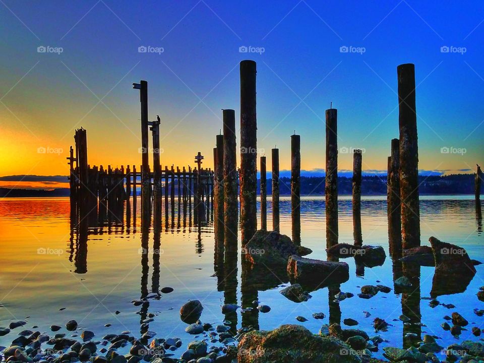 A beautiful sunset viewed off the side of the water with reflections of old pilings on the surface.