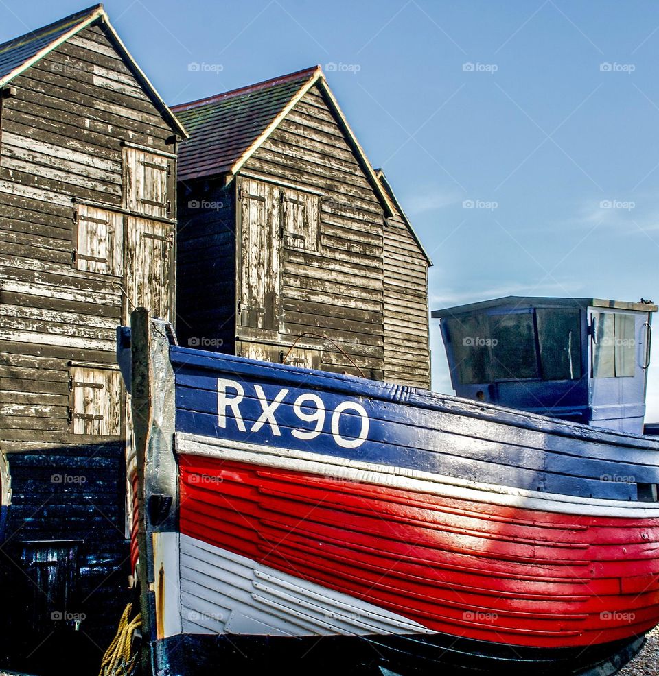 Wooden fishing vessel RX90 in front of tall wooden net huts at Rock-a-nor, Hastings UK