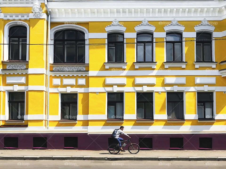 Young man riding a bicycle and using mobile phone in front of the old building in empty city 