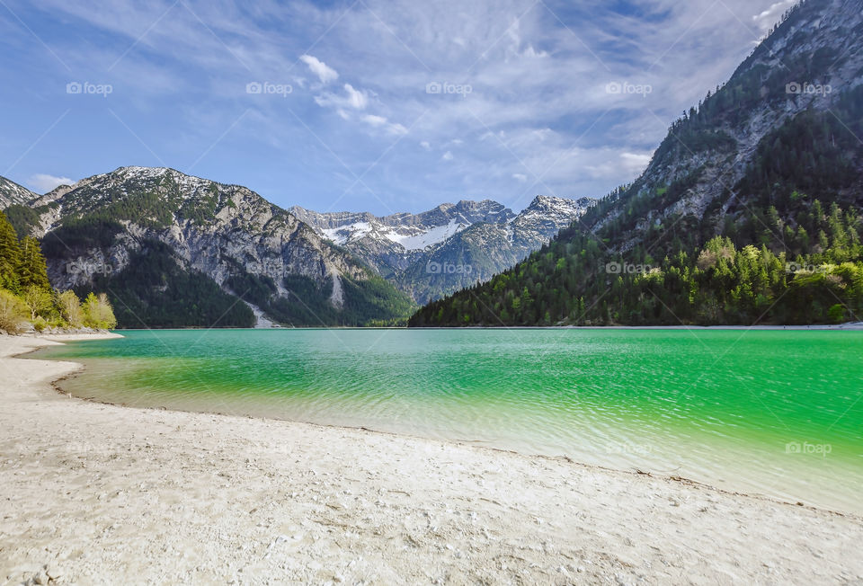 Beautiful landscape view of peaceful lakeside beach with green water in lake and mountains on background with no one 