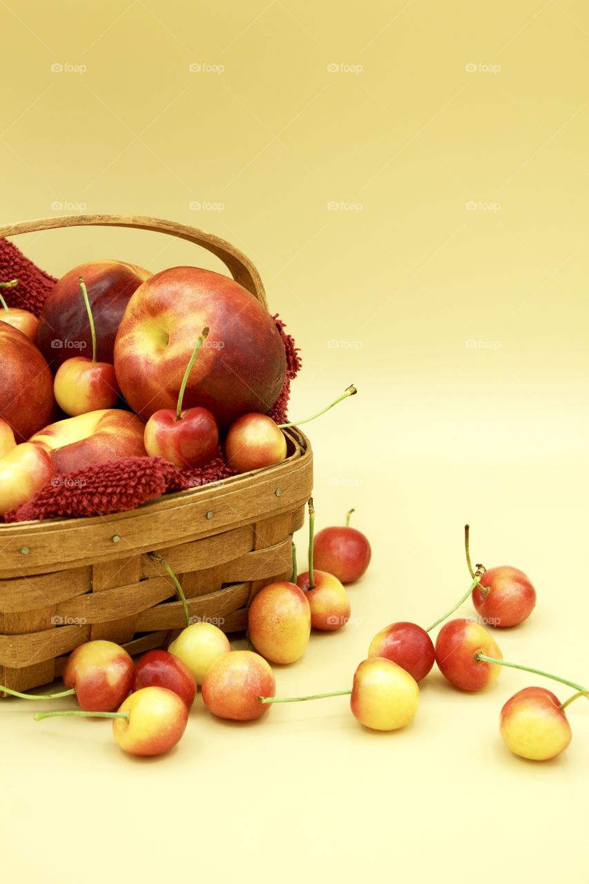 Fruits! - Nectarines And Rainer cherries in a wooden basket against a yellow background 