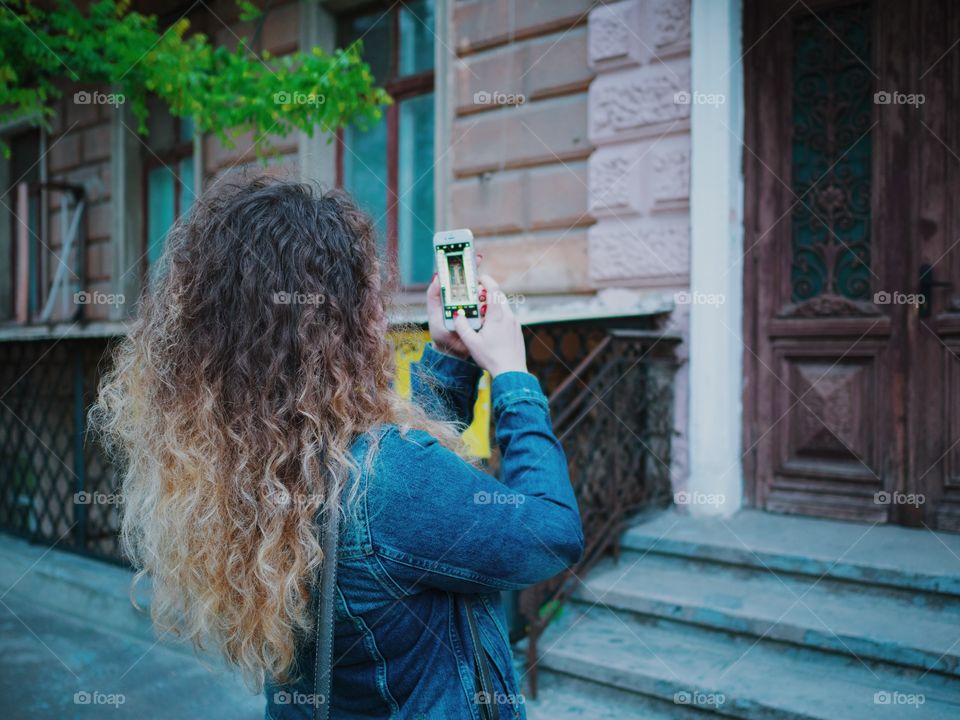 Curly haired woman using her mobile camera for photographing street door