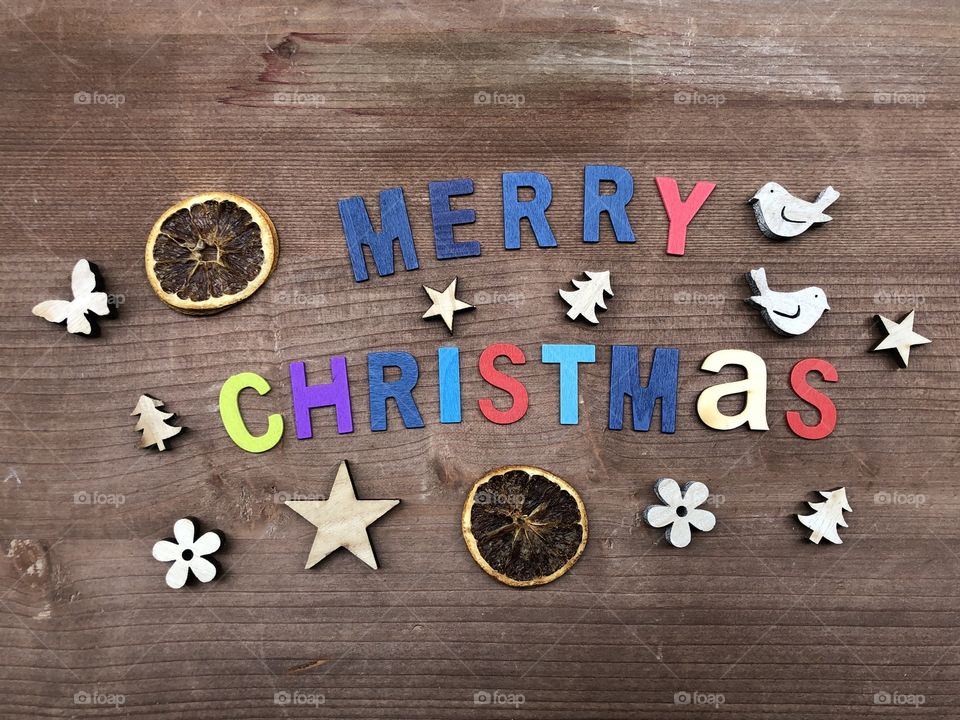 Merry Christmas text composed with colored wooden letters over a wooden board with wooden objects