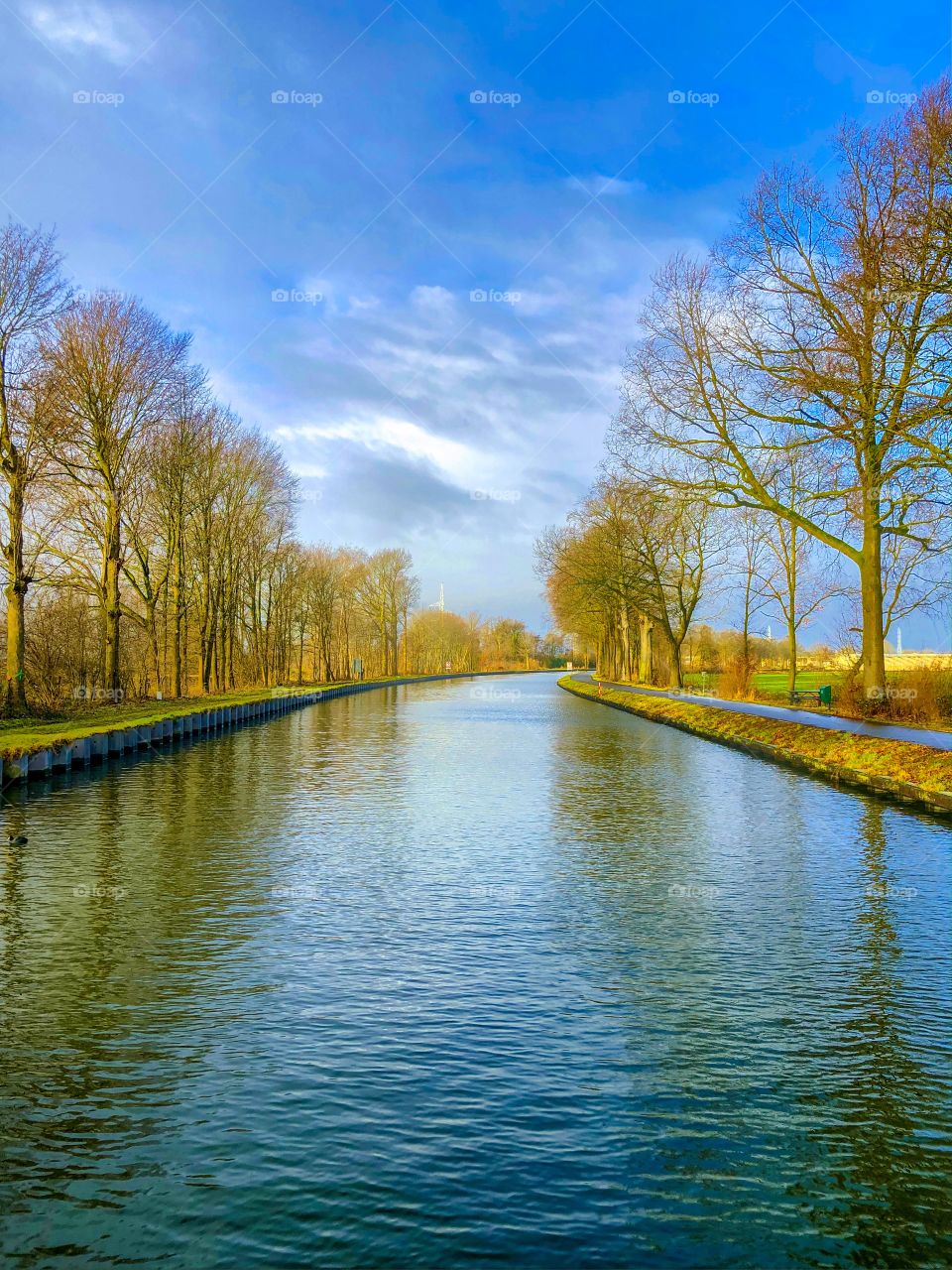 Blue sky on a winters day over the river or canal with a line of trees next to it