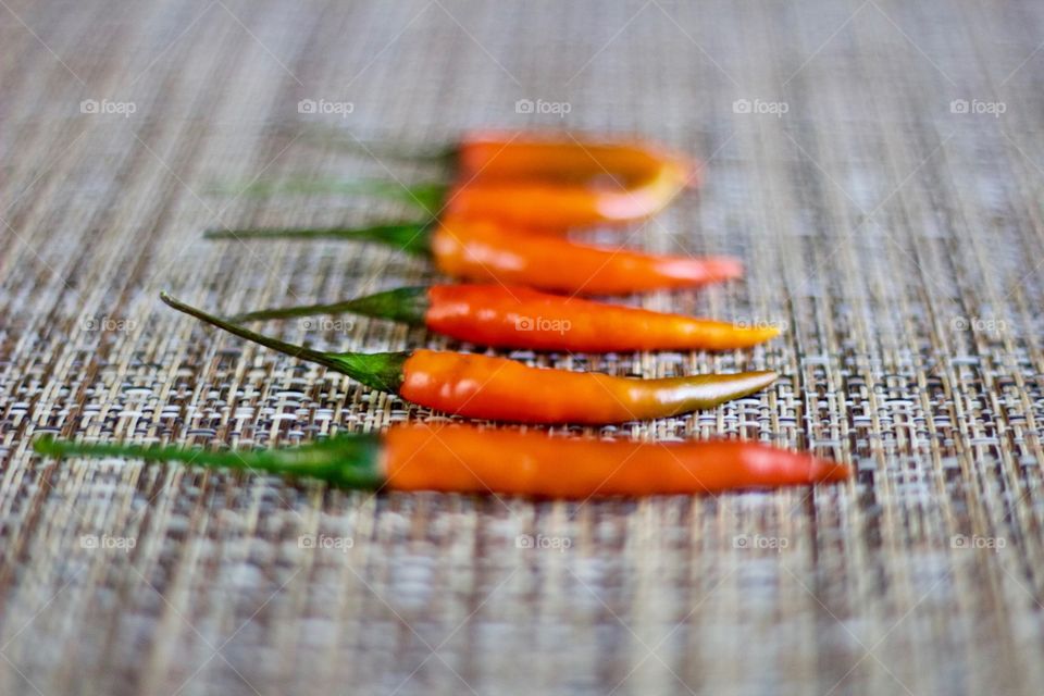Angled view of Thai Bird’s Eye / Thai Bird Chili peppers on a woven neutral background