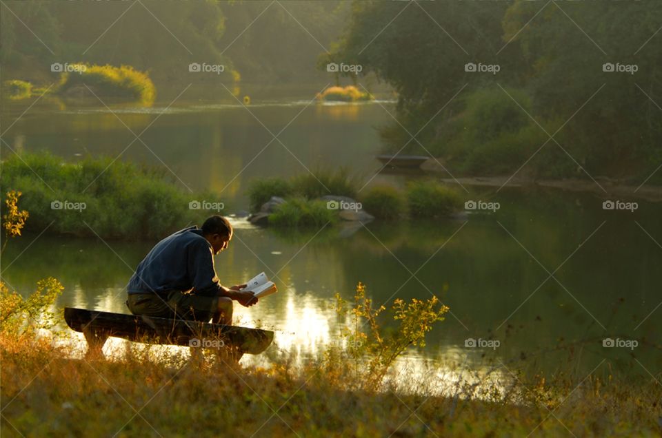 Young man relaxing & reading books alone enjoying his leisure in early winter afternoon