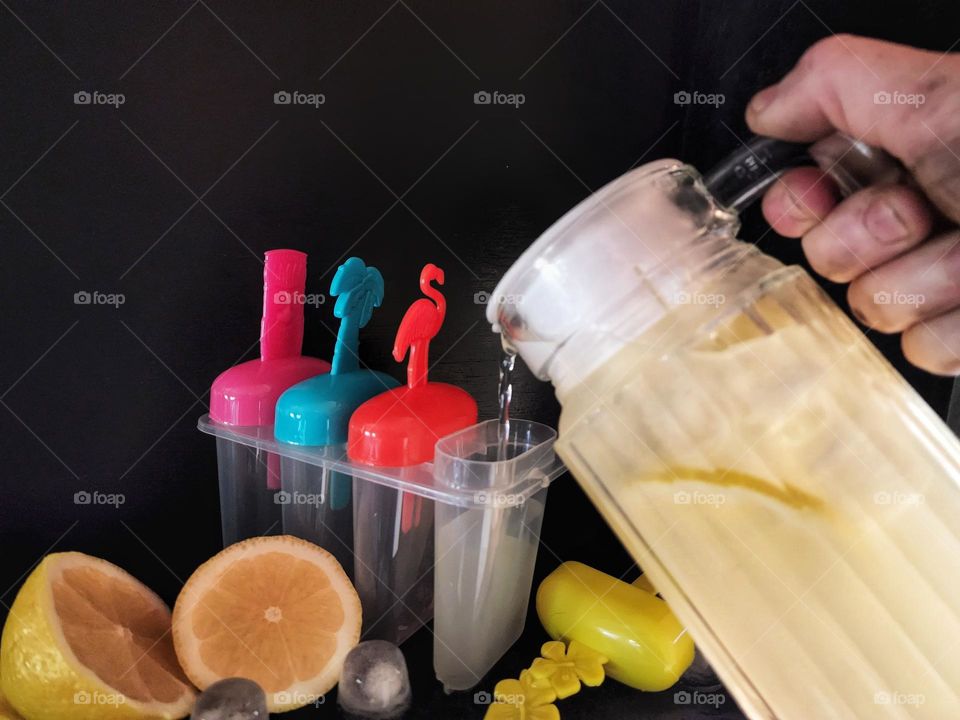 Pouring lemonade into popsicle moulds to make homemade Popsicles.