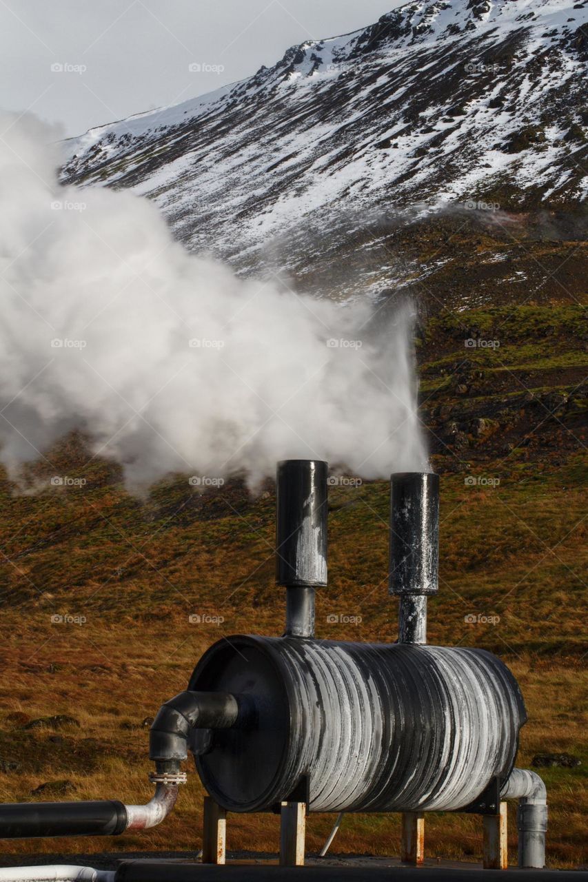 A steam producing machine on the backdrop of snow-covered mountains in Iceland.