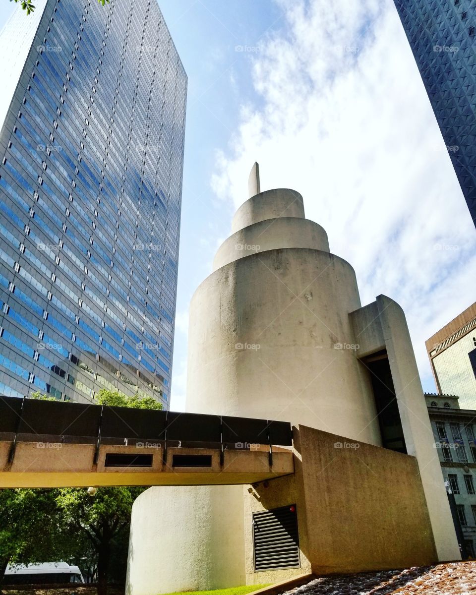 Spiraling white stone tower between skyscrapers against blue sky in downtown Dallas
