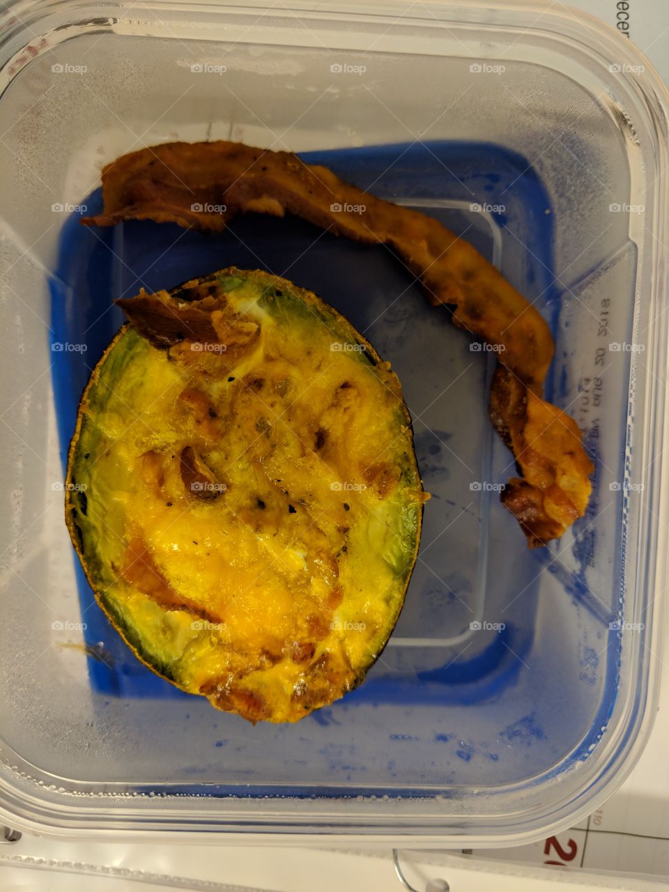 baked avocado with egg crumbled bacon cheese and a slice of bacon