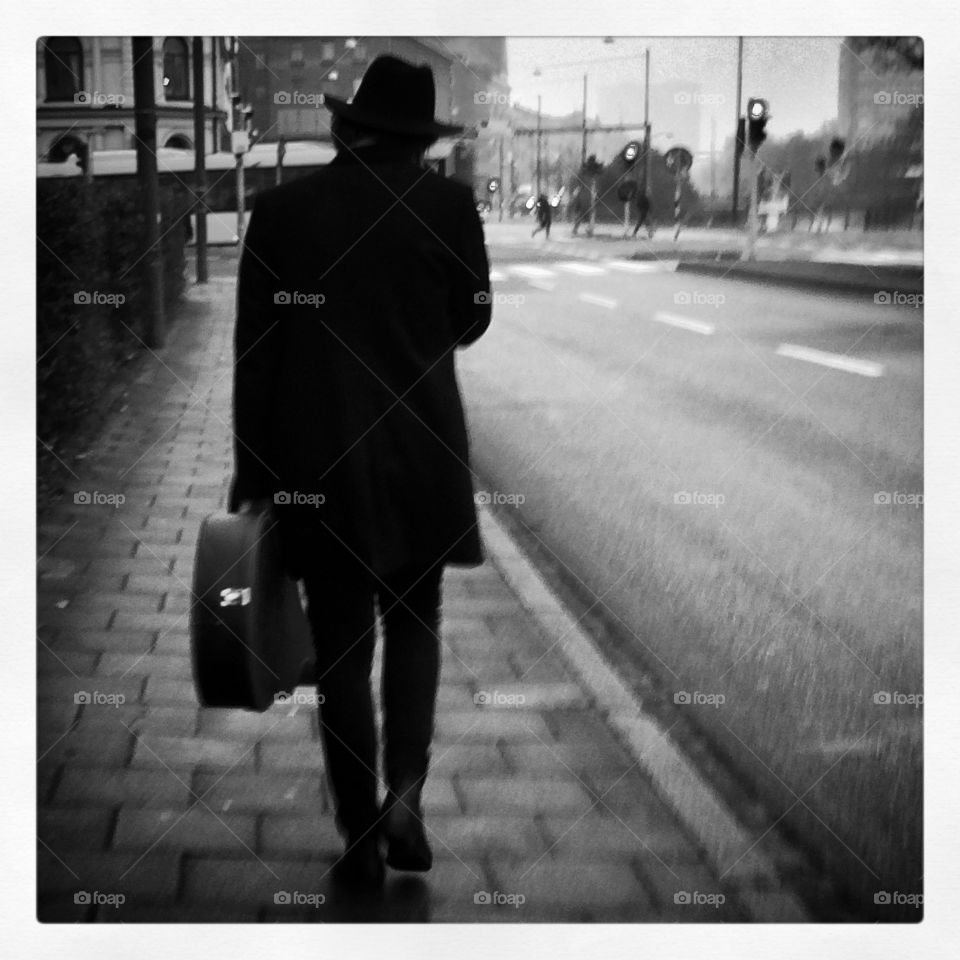 Man with guitar. Black and white documentary photo of an artist with his guitar walking the streets