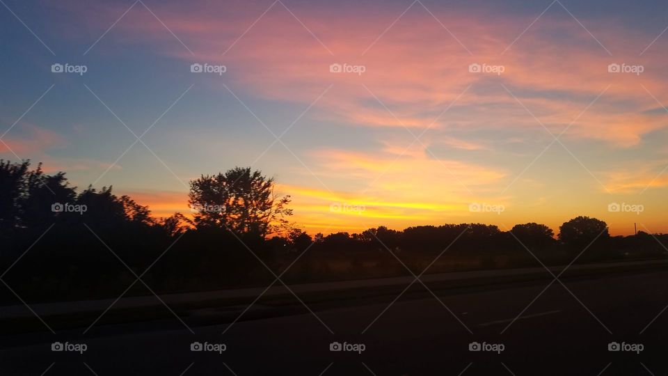 Beautiful sunset in the Kansas backroads. The sun is below the horizon, lighting the sky on fire with orange and yellow. Pink clouds streak across the sky.