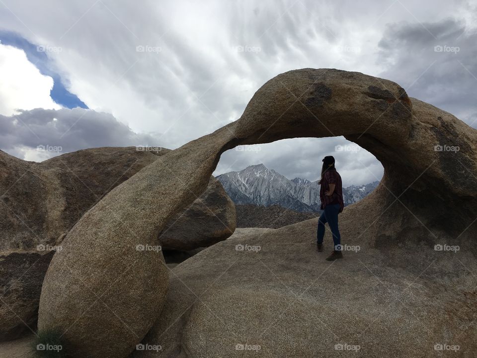 Female hiker peers at the looming Mt. Whitney in the distance from the Mobius Arch in the Alabama Hills. 