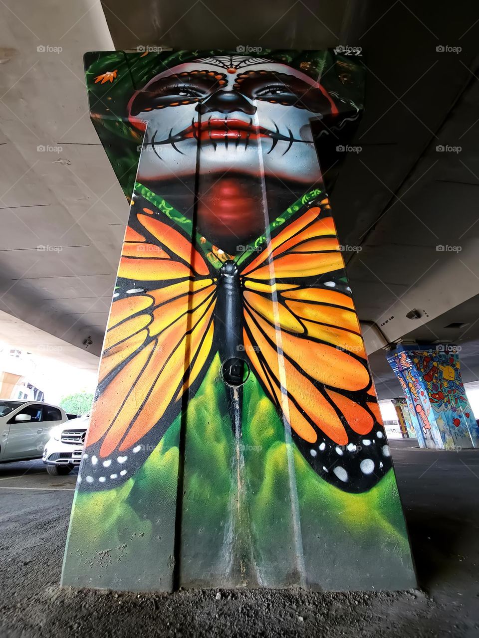 Street art:  Dia de los muertos portrait with a large monarch butterfly on a cement highway pillar underpass.  Also known as day of the dead, a Mexican cultural celebration and remembrance of those that have passed.  Street art artist: @PauLGars0n13