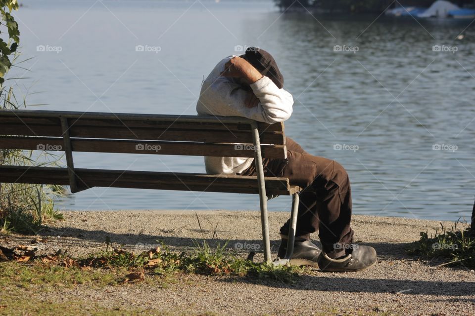 Man Sitting Outdoors. Man sitting on bench outdoors with head down and covering his face with his arms