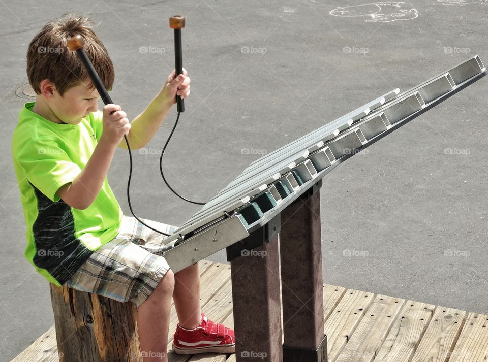 Young Street Musician. Young Boy Playing A Large Metal Xylophone
