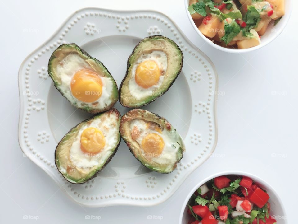 Breakfast Time Shots - flat lay of eggs baked in avocado halves on white plate, pico de gallo and mango salsa in white bowls, white background