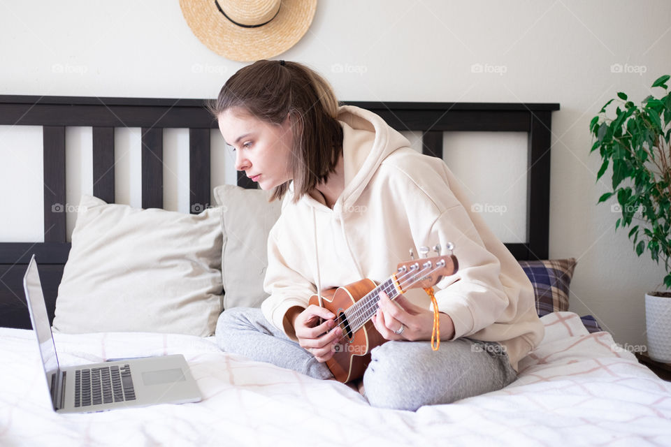 Woman learning how to play ukulele guitar via laptop 