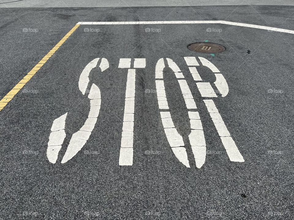 White large street letters painted to say stop for the cars on the road.  Gray, dirty pavement in the city 