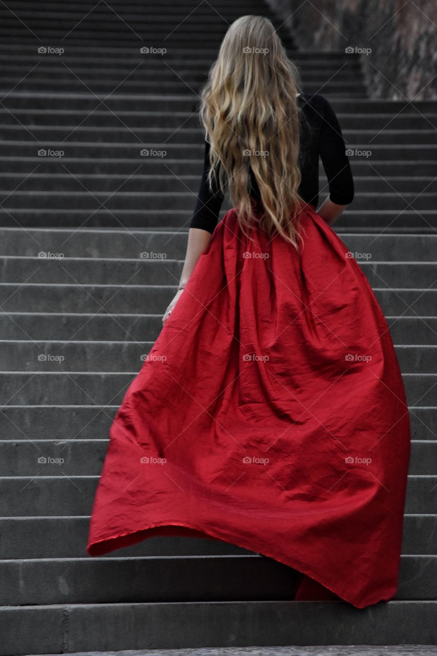 Blonde long hair woman in long red skirt standing on the stairs in old Prague