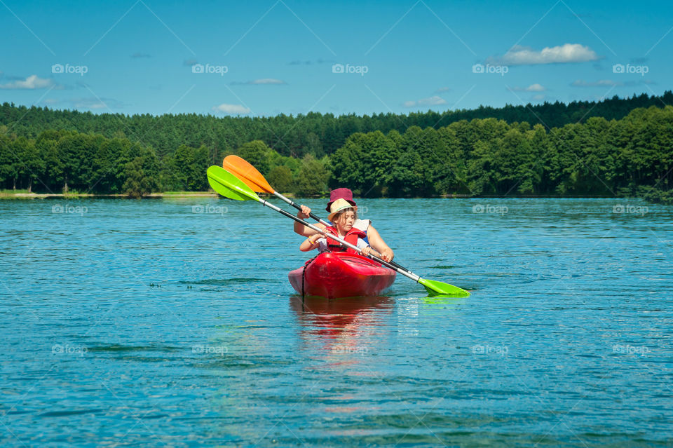 Little girl in red kayak on lake. Beautiful summer.