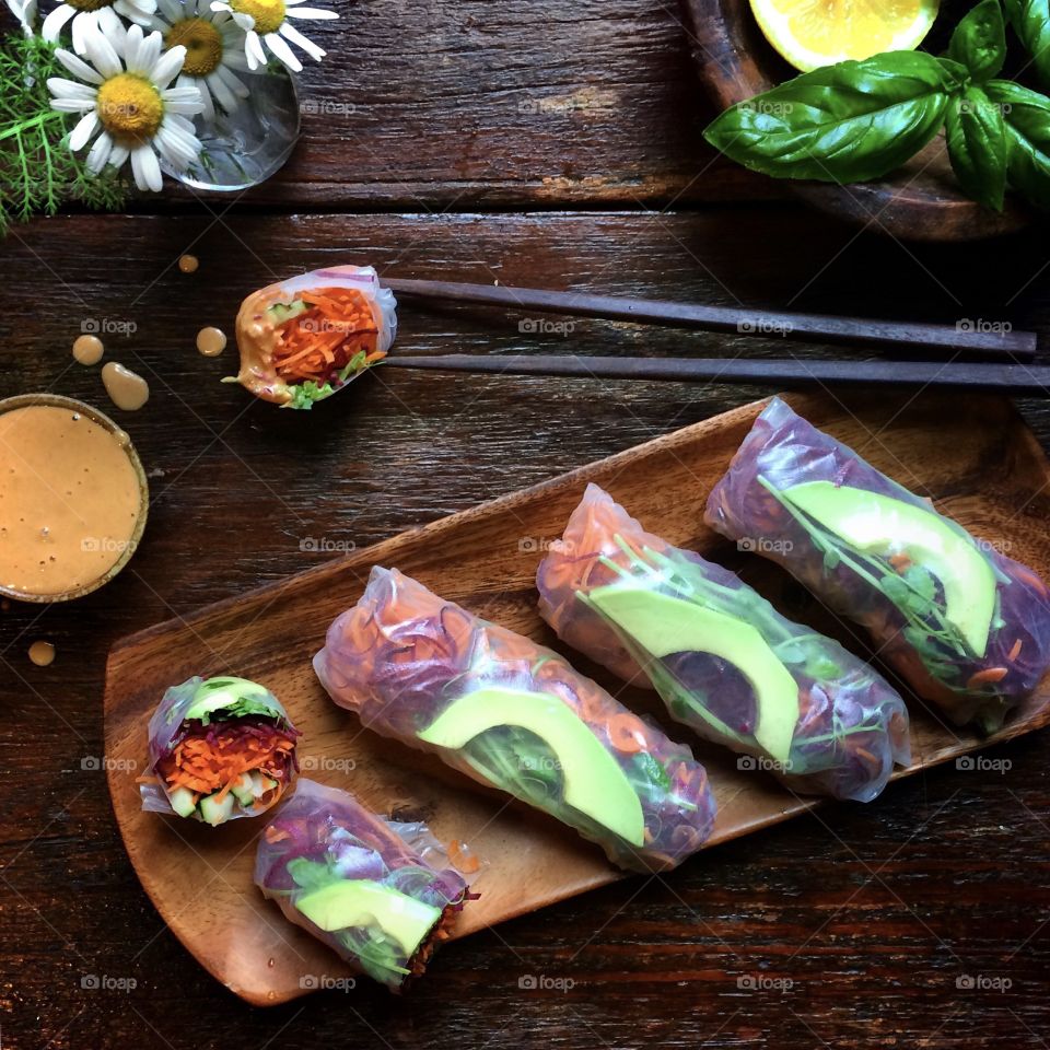 Summer rolls with avocado slices and dipping sauce on a wooden tray with chopsticks.
