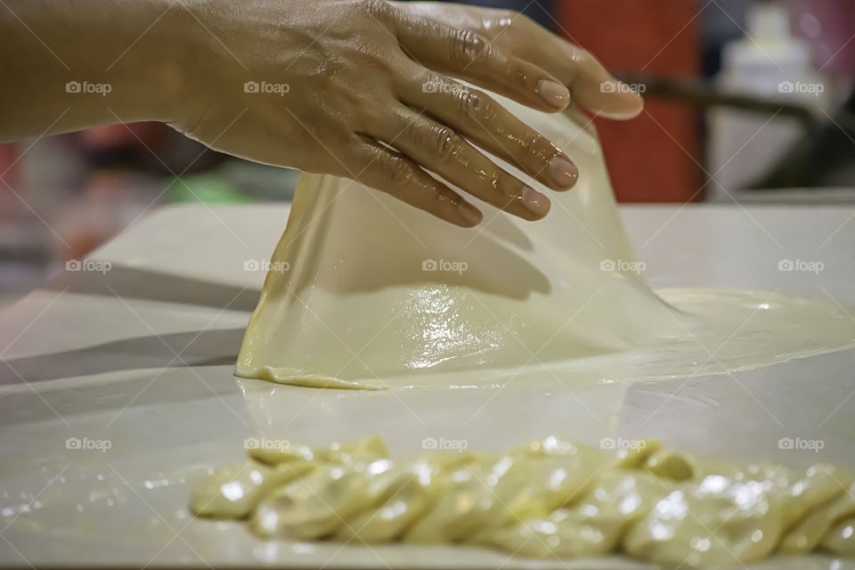 Hands kneading dough to a sheet on the table.