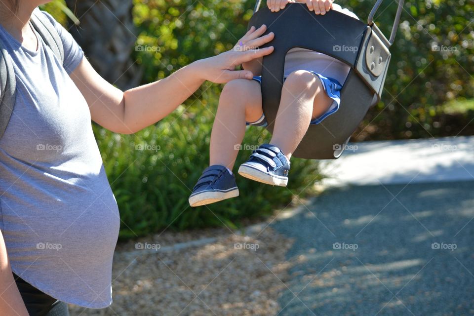Close-up of pregnant mother pushing toddler on swing