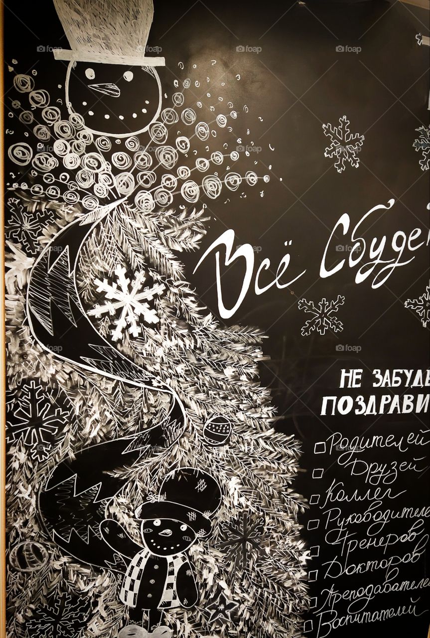 New Year's drawing with chalk on a black board: a snowman, branches of a Christmas tree and wishes for the coming New Year