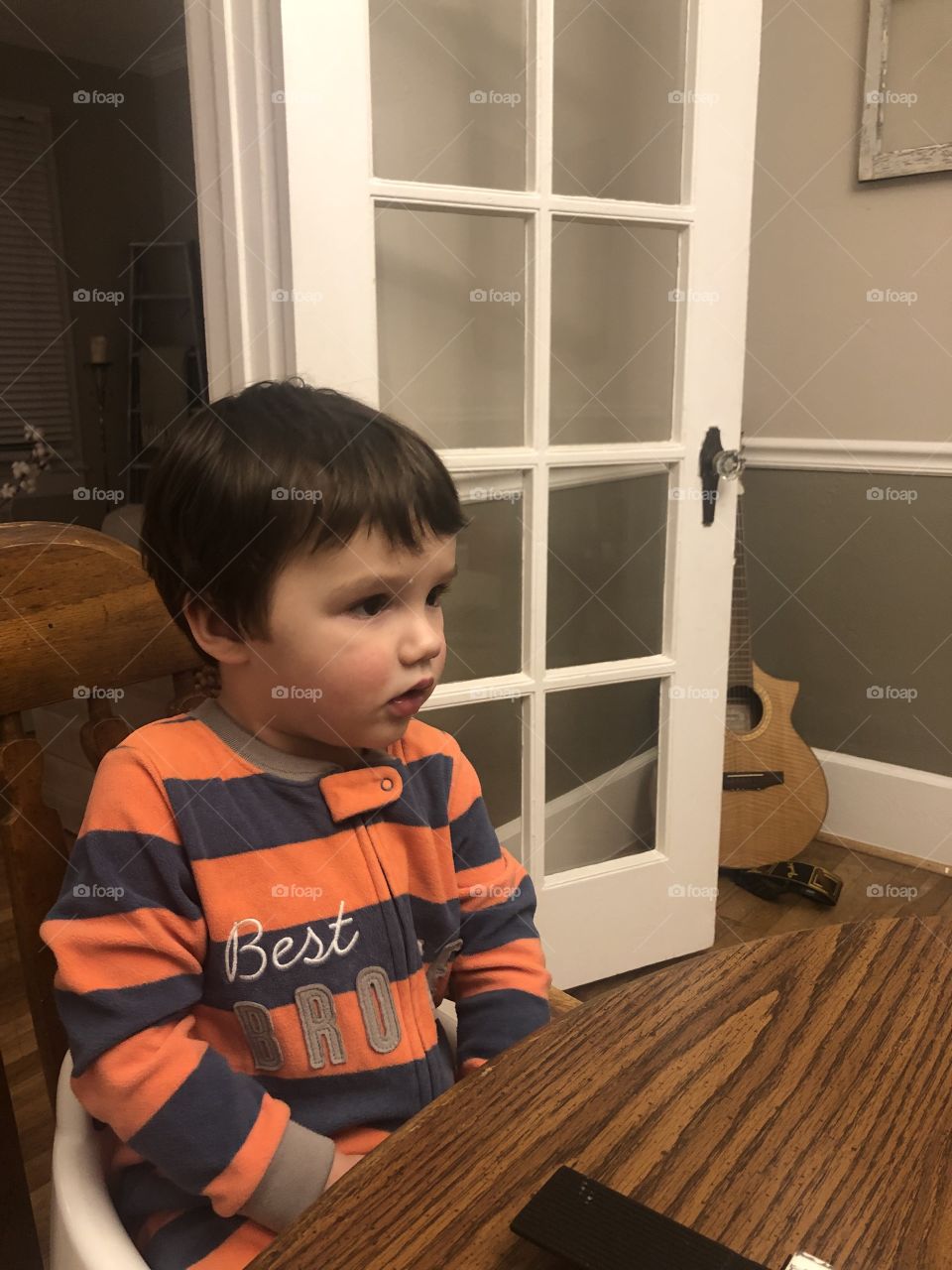 A real cute dark headed two year old in striped pj’s sitting at table. 