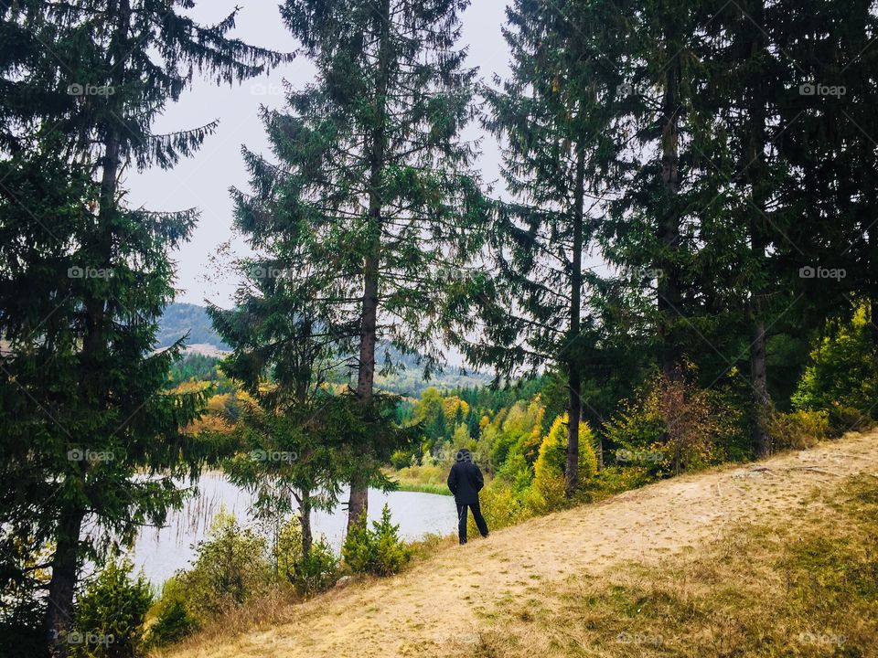 Man dressed in black standing near tall pine cone trees