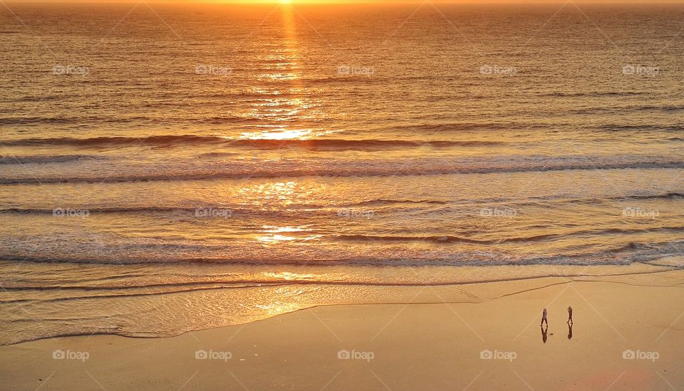 Two walking on a beach at sunset time. 