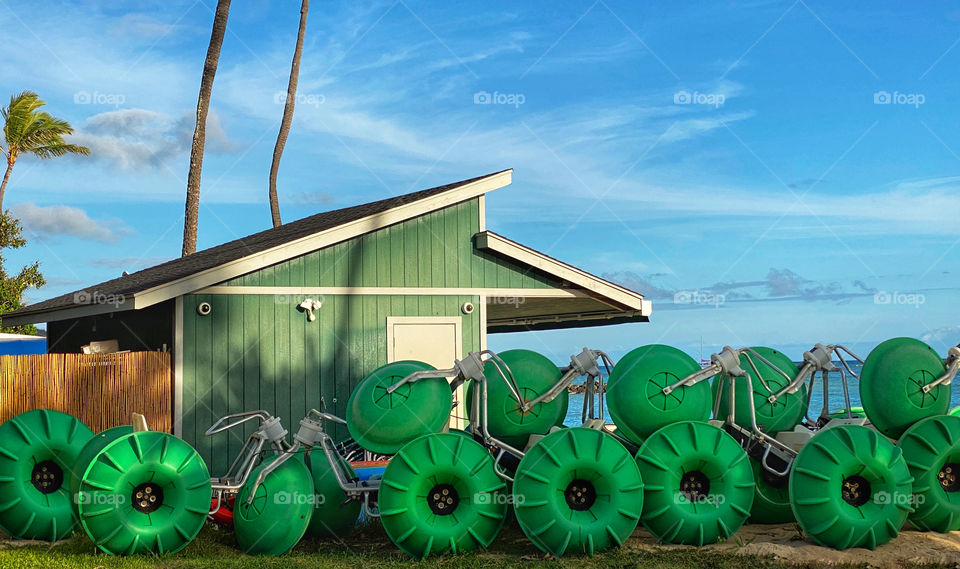Green water tricycles stacked alongside a green storage shed