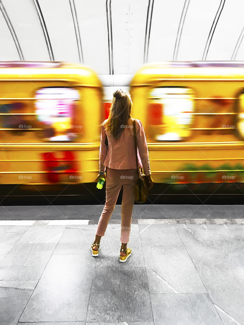 Young woman standing in front of a yellow moving train at the city subway station 