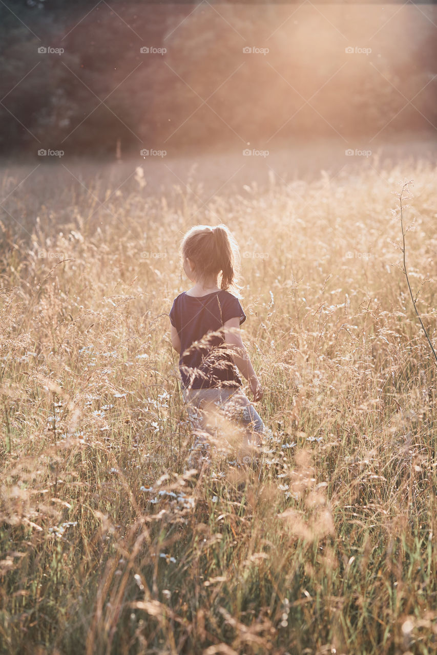 Little happy girl walking through a tall grass in the countryside. Candid people, real moments, authentic situations