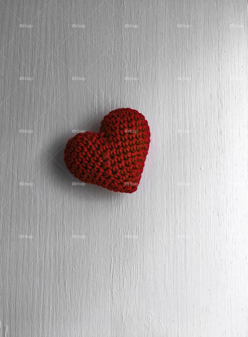 Red knitted heart on a white wooden background, top view