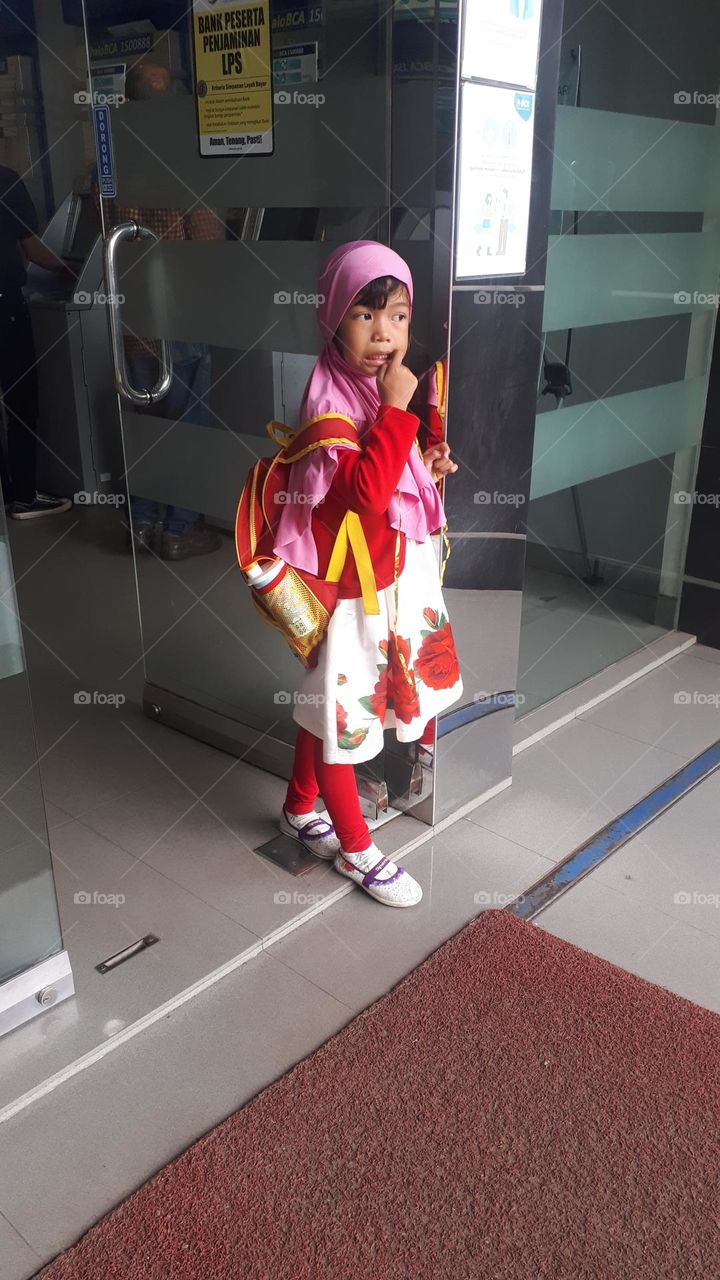 a little girl wearing a hijab and a pink dress is pushing the door out