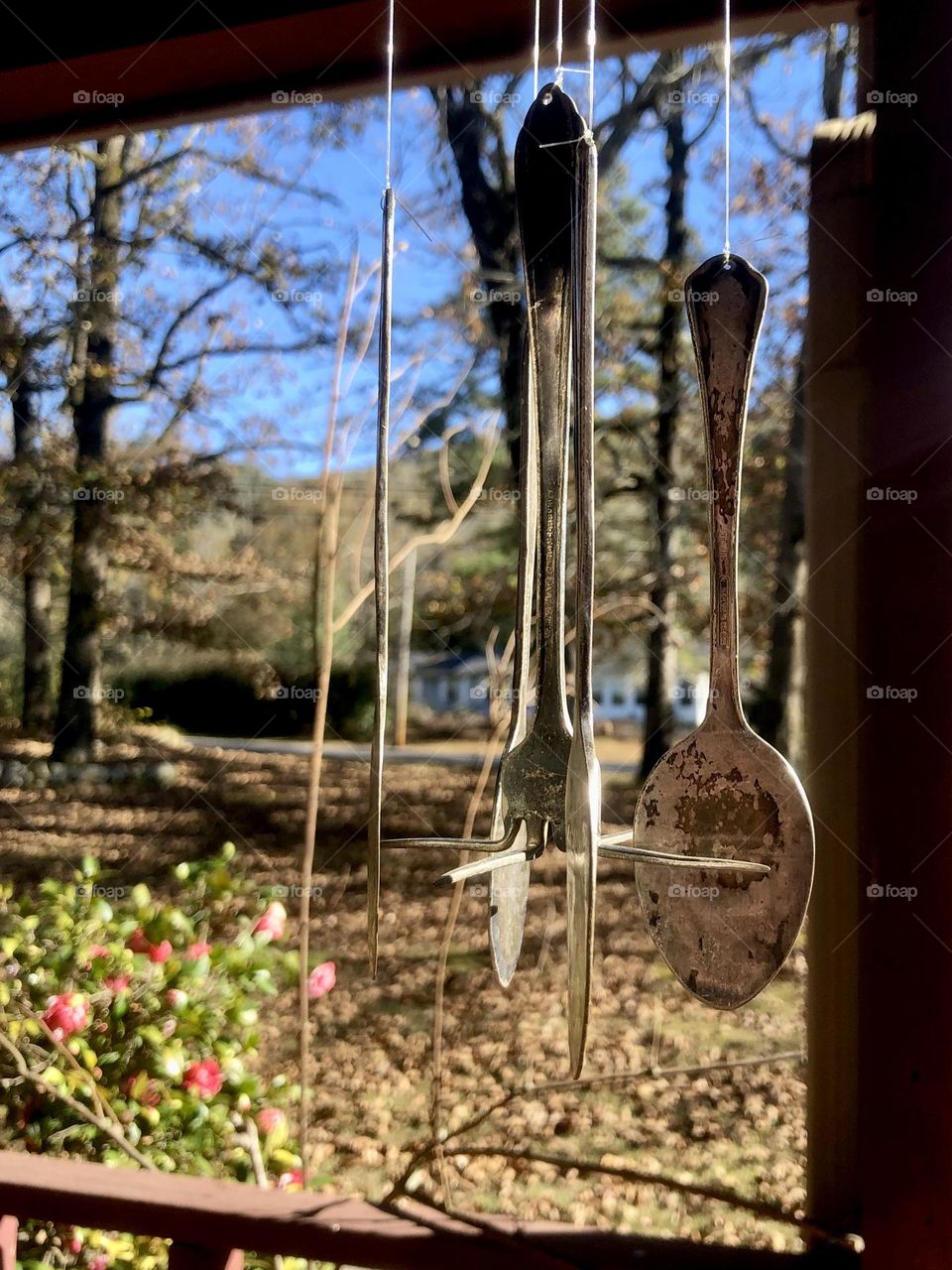 Wind chimes on a sunny porch. The chimes are made of repurposed silverware with a fork in the center position.