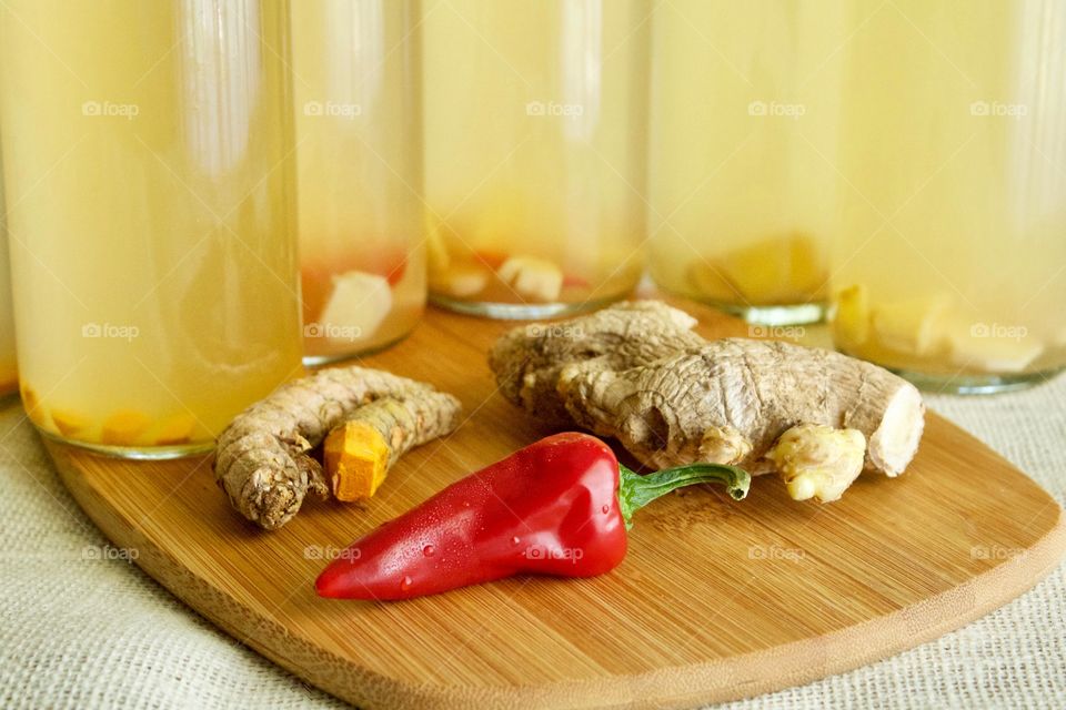 Ingredients to flavor homemade kombucha which is bottled for a second ferment — turmeric root, red chili pepper, and ginger root, on bamboo cutting board