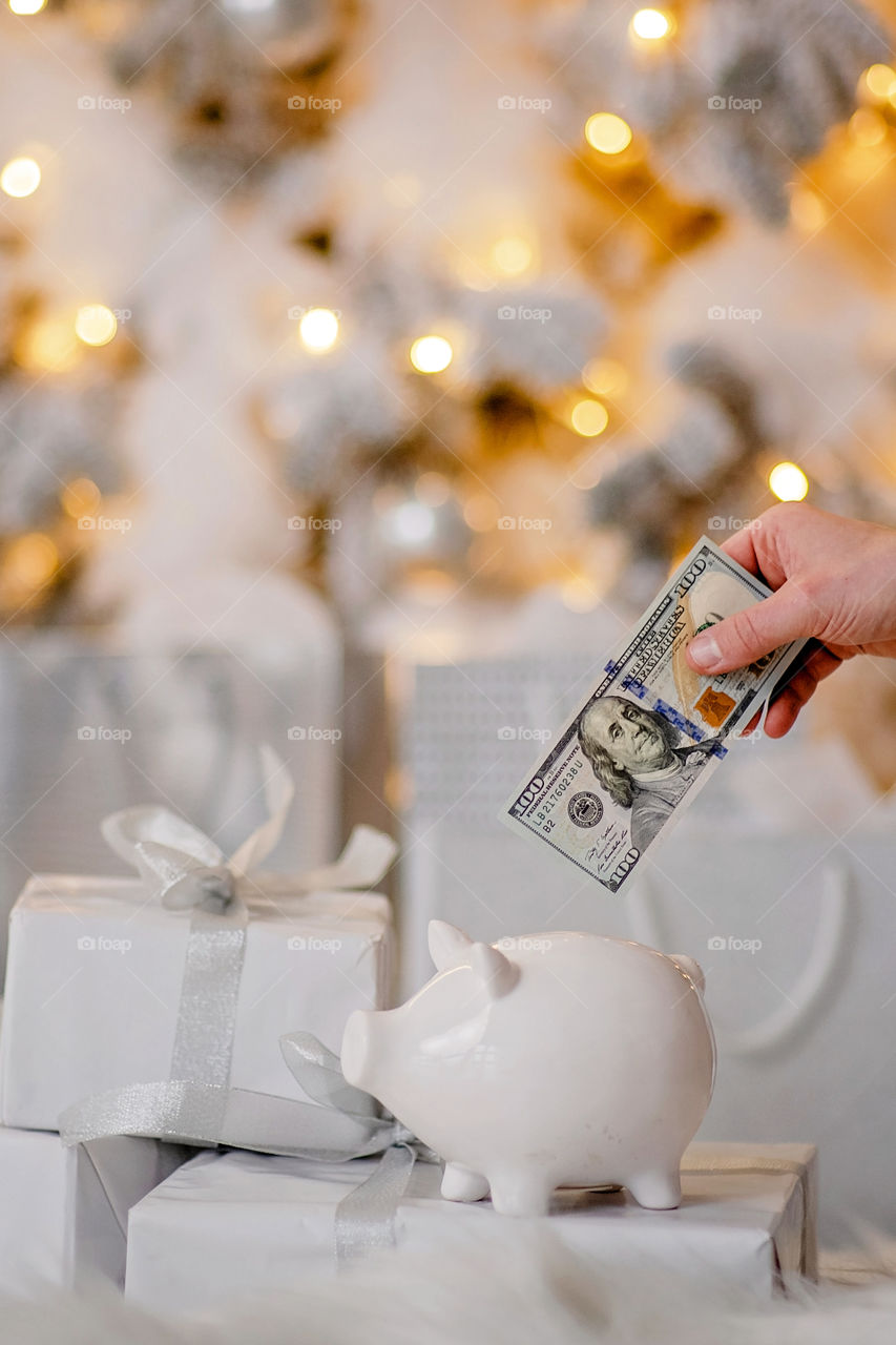 piggy bank with 100 dollars banknote in festive New Year atmosphere of scenery.  Magical bokeh with Christmas tree and bright lights.