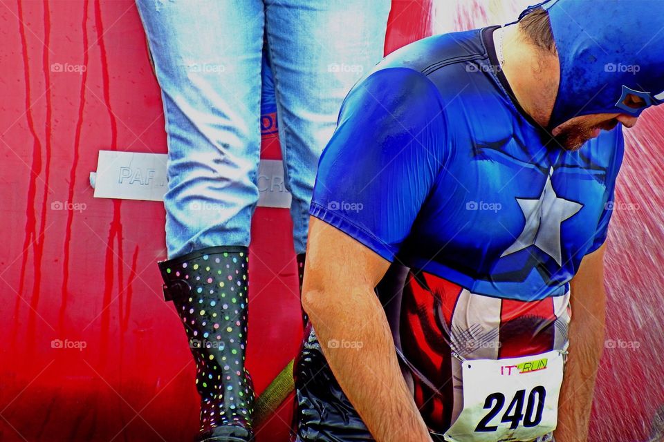 The masked jogger finishing a road race with the cool spray from a firehose on a summer day.