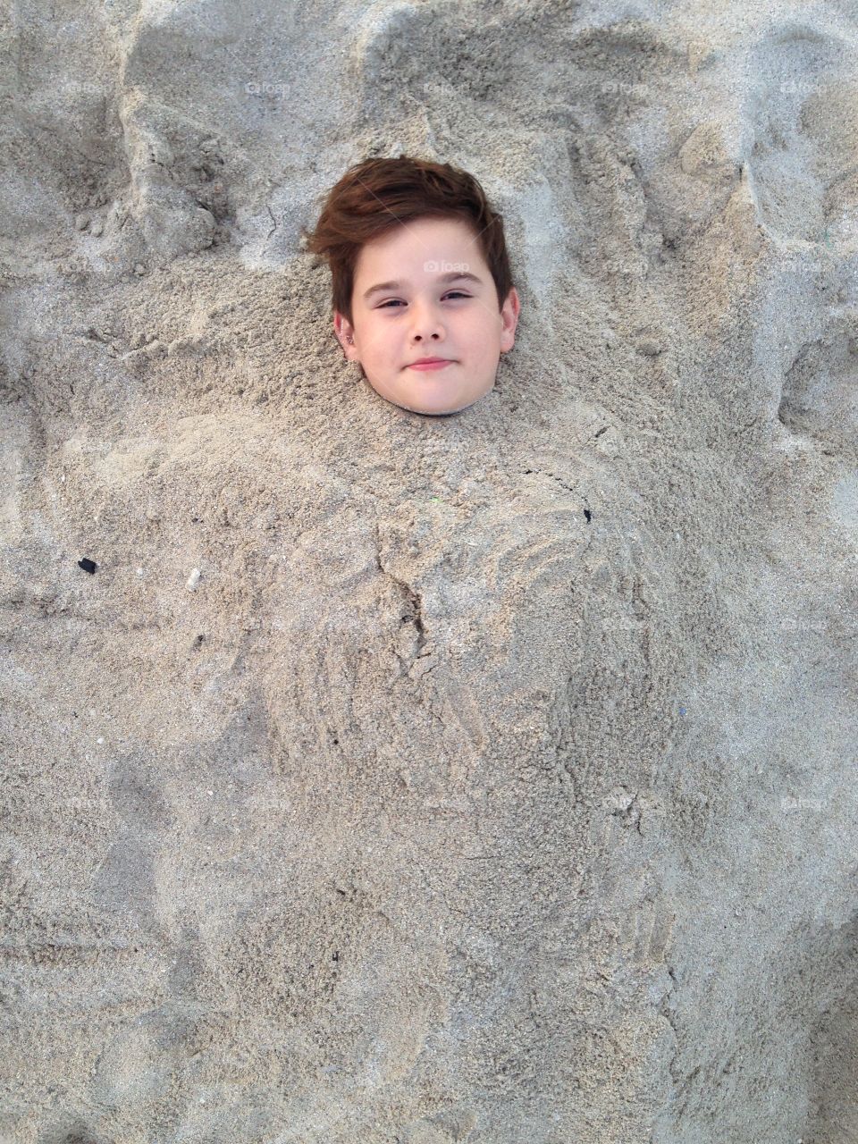Boy buried in sand at beach
