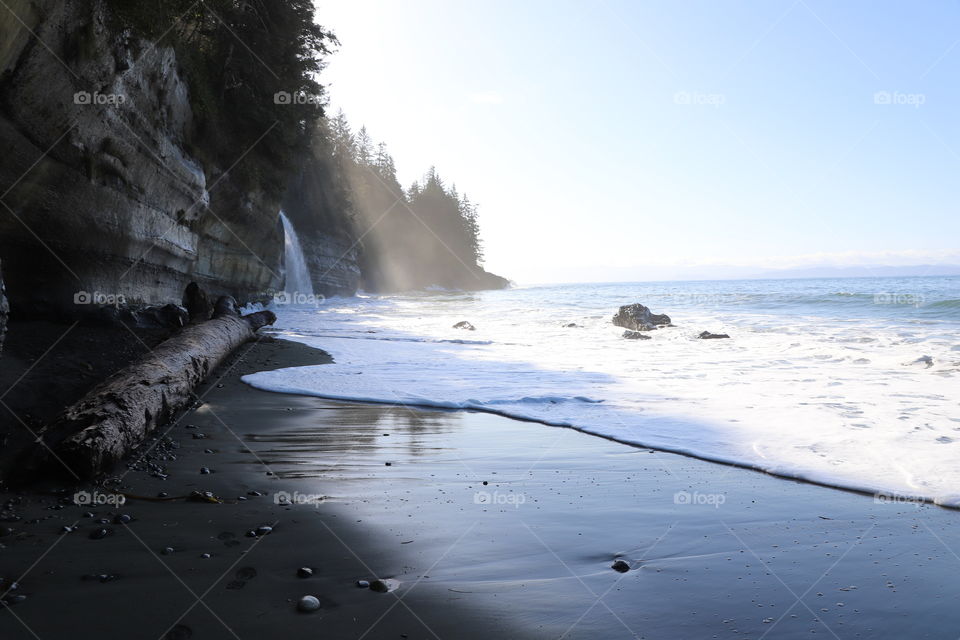 Calm sandy beach during low tide ,crashed waves  slowly bubbling on the shore and waterfall from surrounding forest