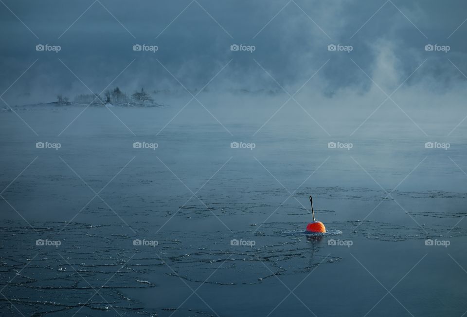 Bright red buoy floating alone in the freezing Baltic Sea in Helsinki, Finland just hours before complete freeze over of the sea on an extremely cold January morning (-20C) on 6 January 2016.