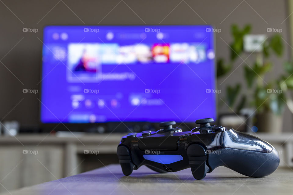 A portrait of PlayStation 4 controller in front of a television displaying the PlayStation home screen.